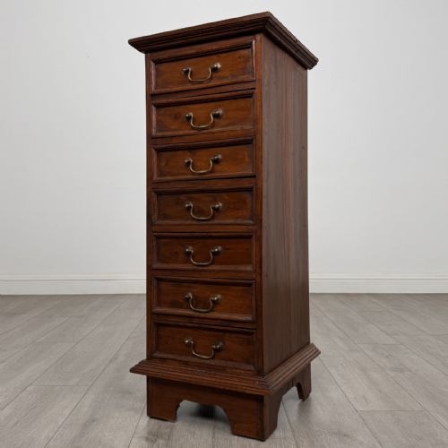 fig 1. A tall and narrow warm brown mahogany chest of drawers with seven stacked drawers and brass drop handles.