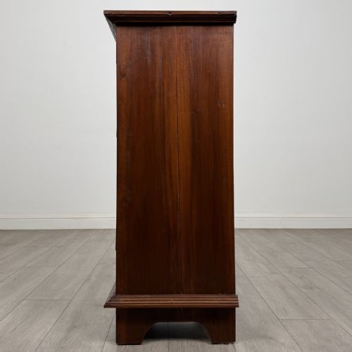 fig 2. A tall and narrow warm brown mahogany chest of drawers with seven stacked drawers and brass drop handles.