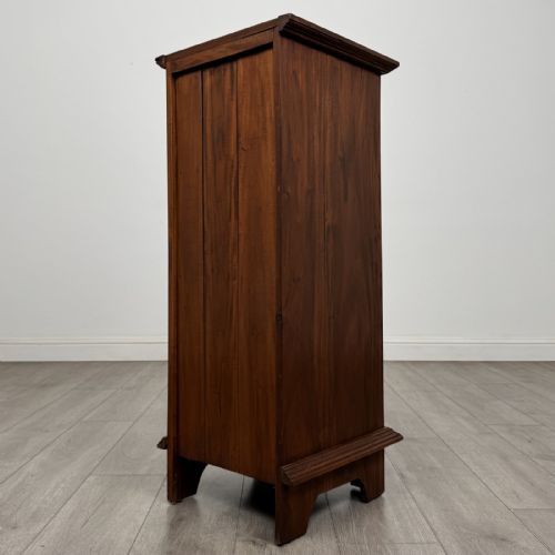 fig 5. A tall and narrow warm brown mahogany chest of drawers with seven stacked drawers and brass drop handles.