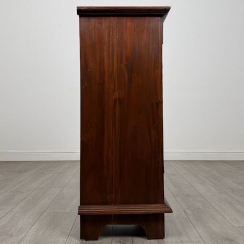 fig 6. A tall and narrow warm brown mahogany chest of drawers with seven stacked drawers and brass drop handles.