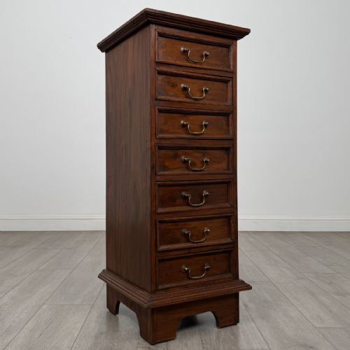 fig 7. A tall and narrow warm brown mahogany chest of drawers with seven stacked drawers and brass drop handles.