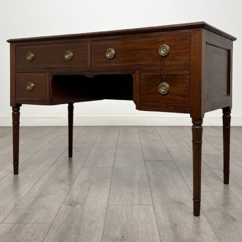 fig 1. An Edwardian mahogany writing table featuring four drawers with brass ring handles, boxwood stringing inlay, a central kneehole aperture, and four slender turned legs.