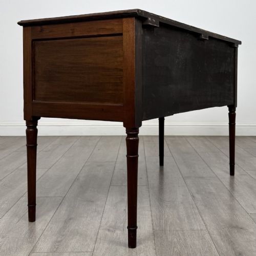 fig 3. An Edwardian mahogany writing table featuring four drawers with brass ring handles, boxwood stringing inlay, a central kneehole aperture, and four slender turned legs.