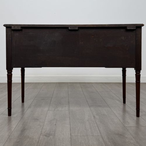 fig 4. An Edwardian mahogany writing table featuring four drawers with brass ring handles, boxwood stringing inlay, a central kneehole aperture, and four slender turned legs.