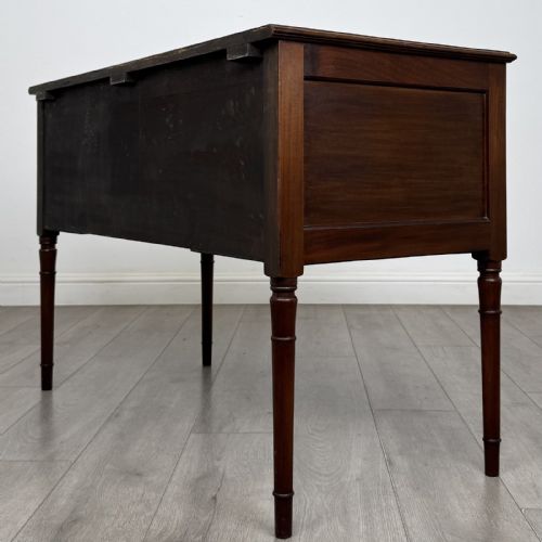 fig 5. An Edwardian mahogany writing table featuring four drawers with brass ring handles, boxwood stringing inlay, a central kneehole aperture, and four slender turned legs.