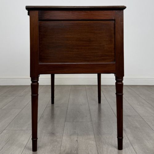 fig 6. An Edwardian mahogany writing table featuring four drawers with brass ring handles, boxwood stringing inlay, a central kneehole aperture, and four slender turned legs.