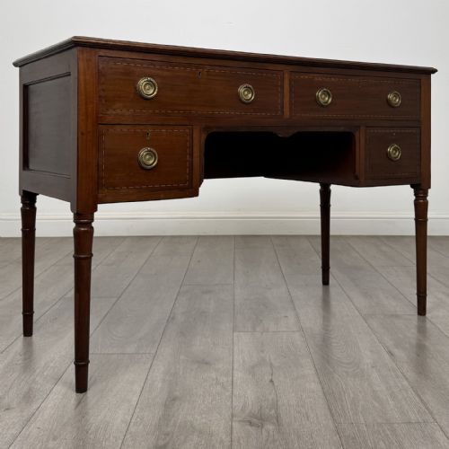 fig 7. An Edwardian mahogany writing table featuring four drawers with brass ring handles, boxwood stringing inlay, a central kneehole aperture, and four slender turned legs.