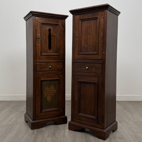 fig 1. A pair of tall dark brown hardwood cupboards featuring a central drawer and panelled doors, with one lower panel decorated with a painted urn motif.