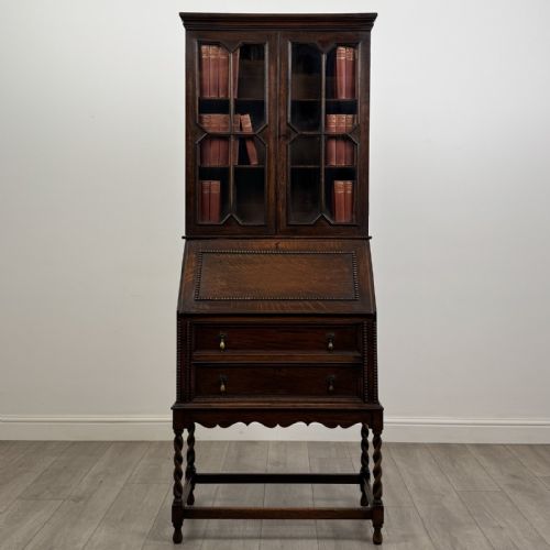 fig 1. A dark oak Jacobean style bureau bookcase featuring twin glazed cabinet doors above a slant-front writing desk with two lower drawers and barley twist legs.