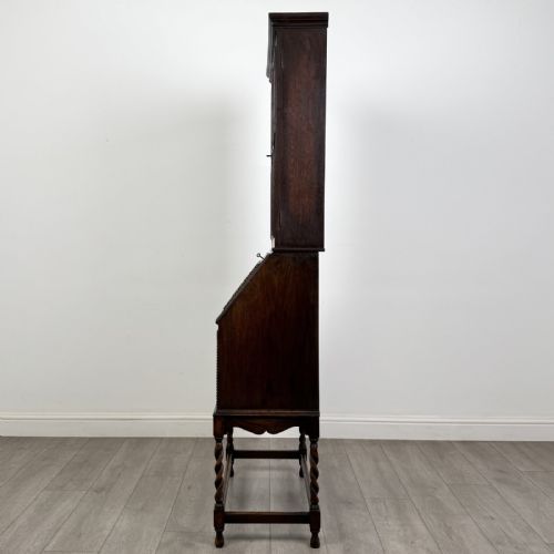 fig 3. A dark oak Jacobean style bureau bookcase featuring twin glazed cabinet doors above a slant-front writing desk with two lower drawers and barley twist legs.