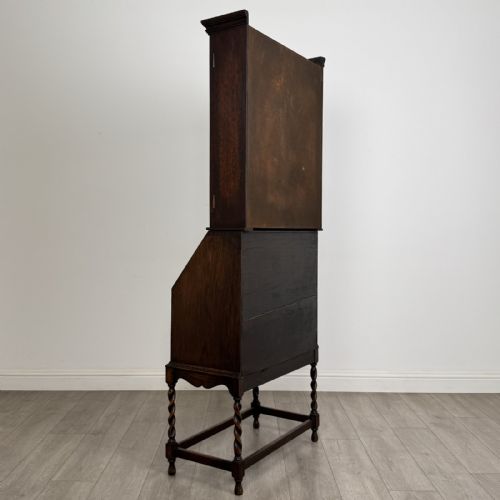 fig 4. A dark oak Jacobean style bureau bookcase featuring twin glazed cabinet doors above a slant-front writing desk with two lower drawers and barley twist legs.