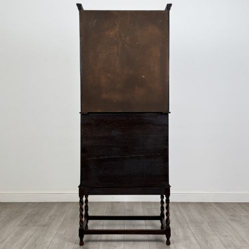 fig 5. A dark oak Jacobean style bureau bookcase featuring twin glazed cabinet doors above a slant-front writing desk with two lower drawers and barley twist legs.
