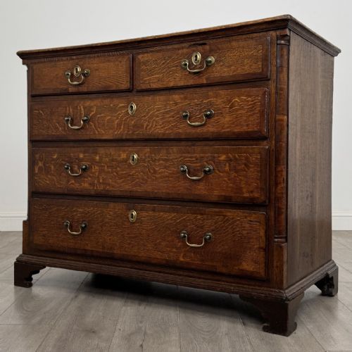 fig 1. An eighteenth-century Georgian oak chest of drawers featuring two short drawers over three long drawers with brass swan-neck handles and bracket feet.