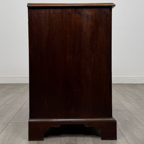 fig 6. An 18th-century dark mahogany low cupboard featuring twin panelled doors with brass keyhole escutcheons resting on bracket feet.