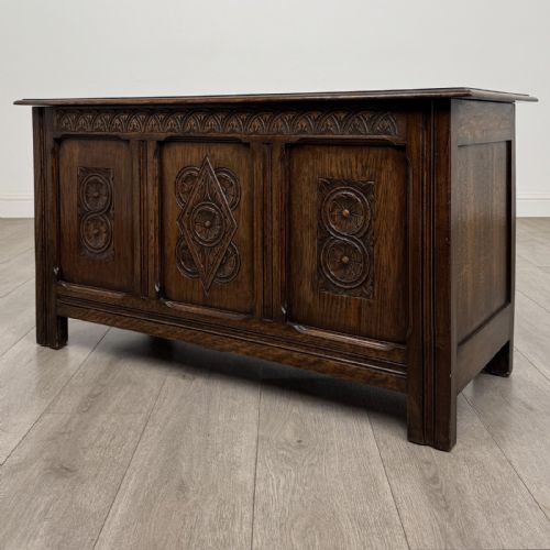 fig 1. A dark oak Jacobean style blanket box featuring a carved lunette frieze across the top rail and three panelled sections with geometric lozenge and rosette motifs.