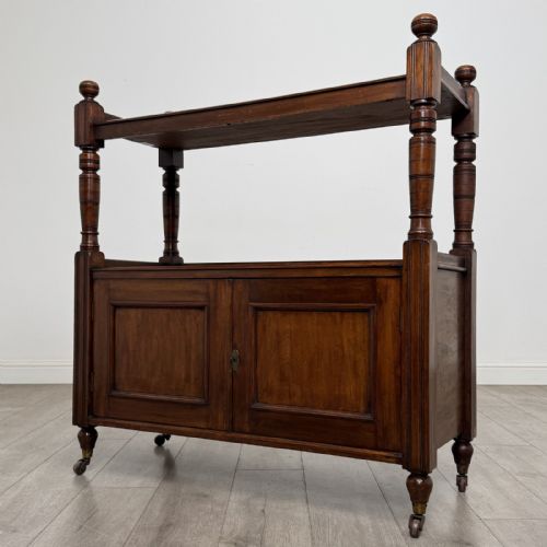 fig 1. A Victorian mahogany buffet trolley featuring an upper open shelf supported by turned column pillars over a lower two-door panelled cupboard set on brass castors.
