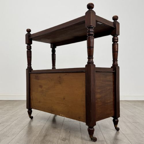 fig 5. A Victorian mahogany buffet trolley featuring an upper open shelf supported by turned column pillars over a lower two-door panelled cupboard set on brass castors.