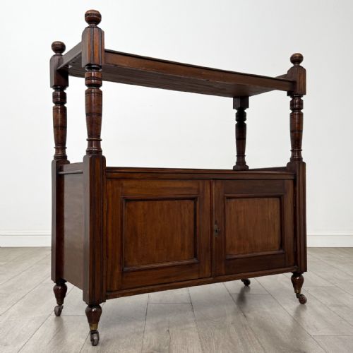 fig 7. A Victorian mahogany buffet trolley featuring an upper open shelf supported by turned column pillars over a lower two-door panelled cupboard set on brass castors.