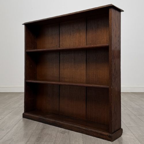 fig 1. A low Edwardian solid oak open bookcase featuring three wide shelves and a dark polished finish.