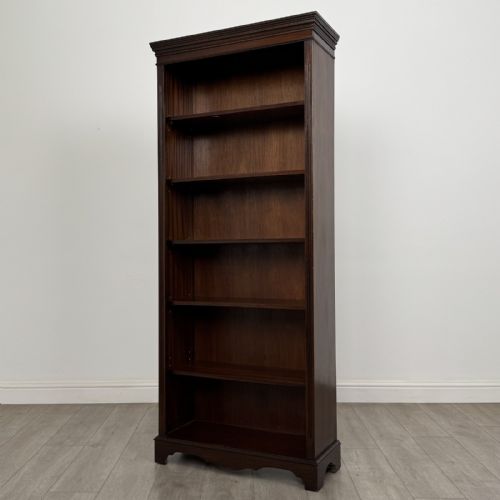 fig 2. A tall dark mahogany open bookcase featuring a dentil cornice, five fixed shelves, fluted side pilasters, and a shaped apron base.