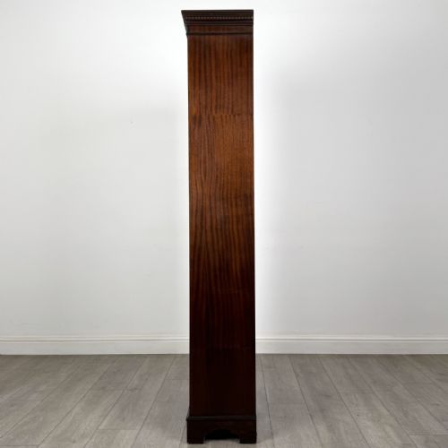 fig 3. A tall dark mahogany open bookcase featuring a dentil cornice, five fixed shelves, fluted side pilasters, and a shaped apron base.