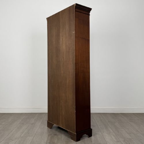 fig 6. A tall dark mahogany open bookcase featuring a dentil cornice, five fixed shelves, fluted side pilasters, and a shaped apron base.