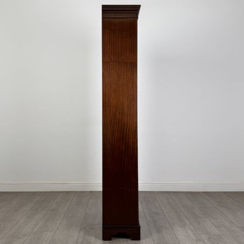 fig 7. A tall dark mahogany open bookcase featuring a dentil cornice, five fixed shelves, fluted side pilasters, and a shaped apron base.