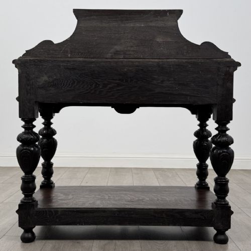 fig 4. A dark carved oak side table featuring a Green Man mask on the front frieze, turned legs, a low undertier, and a raised carved gallery back.