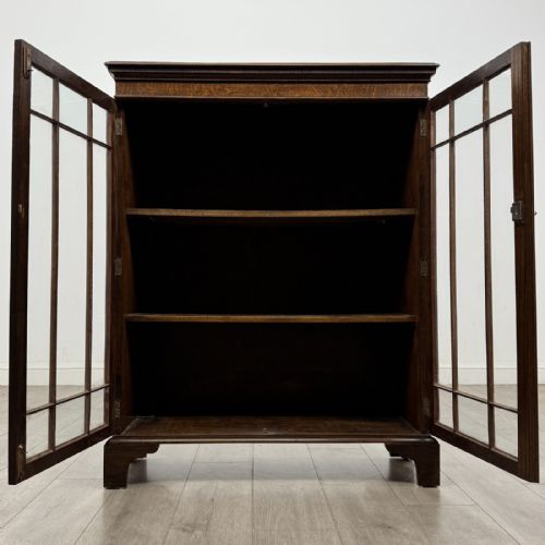 fig 1. A dark oak Georgian style display cabinet featuring twin glazed doors with rectangular timber mullions and bracket feet.