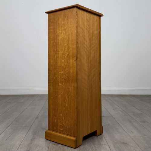 fig 4. A tall, narrow warm oak cupboard featuring a single arched fielded panel door with three brass H-hinges and a small brass door knob.