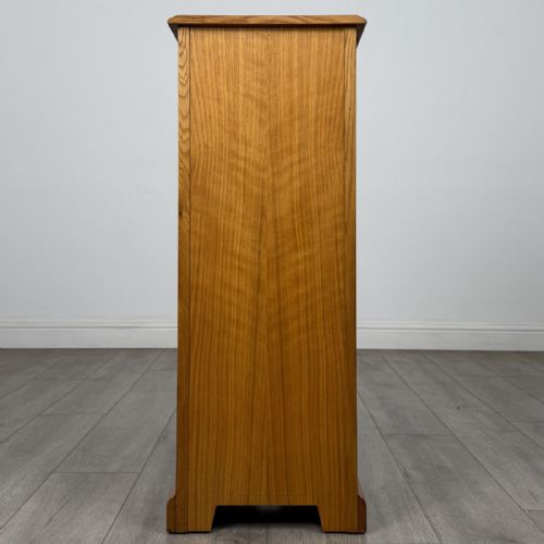 fig 5. A tall, narrow warm oak cupboard featuring a single arched fielded panel door with three brass H-hinges and a small brass door knob.