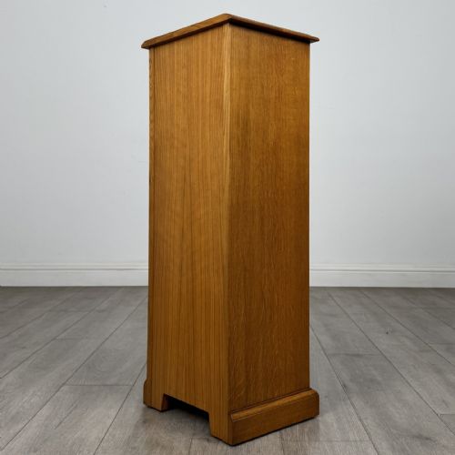 fig 6. A tall, narrow warm oak cupboard featuring a single arched fielded panel door with three brass H-hinges and a small brass door knob.