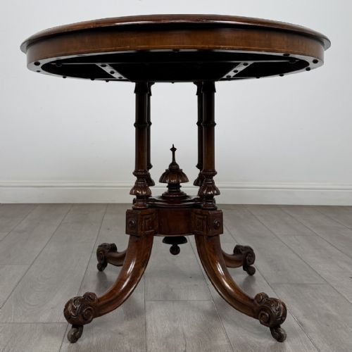 fig 1. A Victorian burr walnut tilt-top loo table featuring an oval top supported by four turned columns and carved quadform legs with scroll feet.