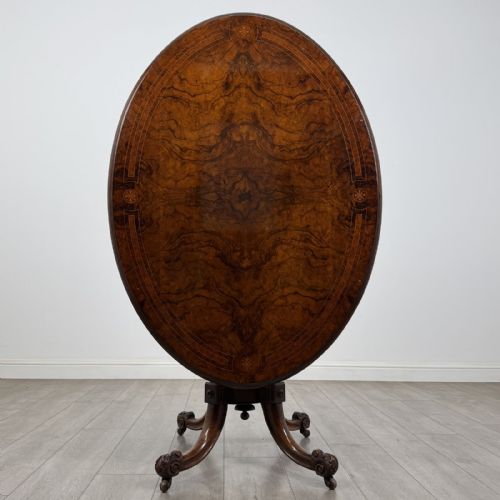 fig 2. A Victorian burr walnut tilt-top loo table featuring an oval top supported by four turned columns and carved quadform legs with scroll feet.