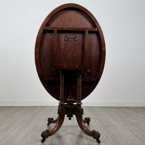 fig 3. A Victorian burr walnut tilt-top loo table featuring an oval top supported by four turned columns and carved quadform legs with scroll feet.