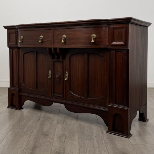 fig 1. An Edwardian dark mahogany bow-front sideboard featuring two drawers with brass drop handles over a double cupboard with carved details.
