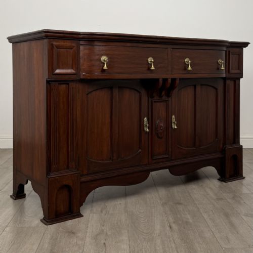 fig 7. An Edwardian dark mahogany bow-front sideboard featuring two drawers with brass drop handles over a double cupboard with carved details.