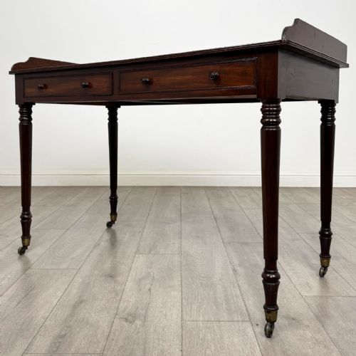fig 1. A dark mahogany Georgian writing desk featuring two frieze drawers with wooden knobs, turned legs on brass castors, and a raised gallery edge.
