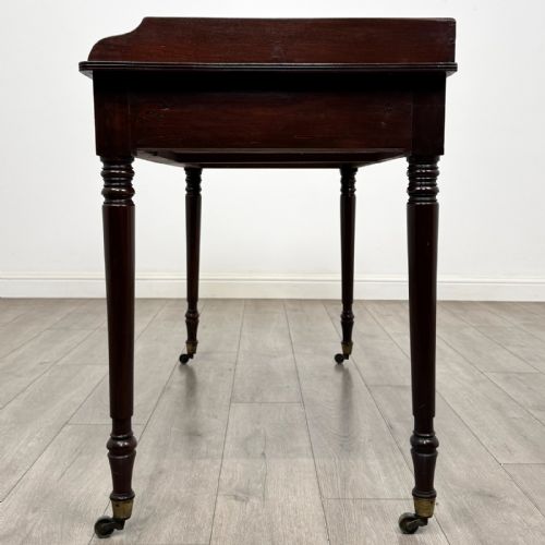 fig 2. A dark mahogany Georgian writing desk featuring two frieze drawers with wooden knobs, turned legs on brass castors, and a raised gallery edge.