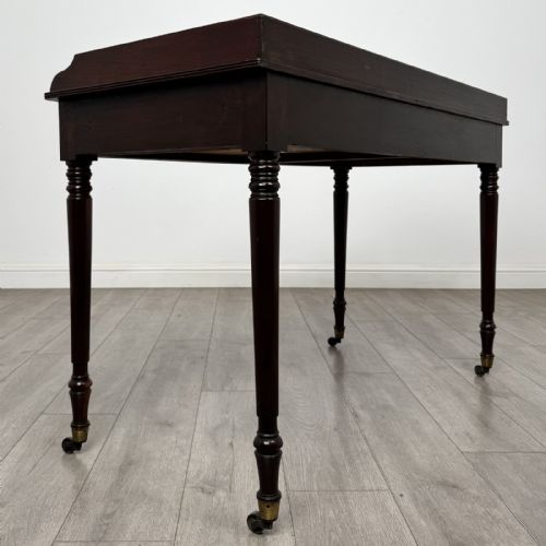 fig 3. A dark mahogany Georgian writing desk featuring two frieze drawers with wooden knobs, turned legs on brass castors, and a raised gallery edge.