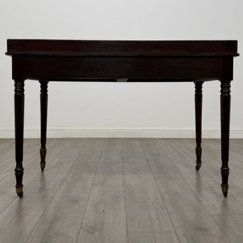fig 4. A dark mahogany Georgian writing desk featuring two frieze drawers with wooden knobs, turned legs on brass castors, and a raised gallery edge.