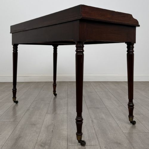 fig 5. A dark mahogany Georgian writing desk featuring two frieze drawers with wooden knobs, turned legs on brass castors, and a raised gallery edge.