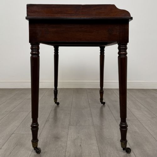 fig 6. A dark mahogany Georgian writing desk featuring two frieze drawers with wooden knobs, turned legs on brass castors, and a raised gallery edge.