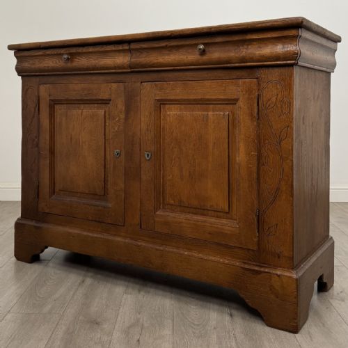 fig 1. An antique French oak sideboard featuring two top drawers above two panelled cupboard doors with carved floral details on the outer edges.
