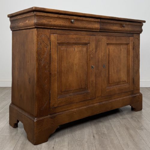 fig 7. An antique French oak sideboard featuring two top drawers above two panelled cupboard doors with carved floral details on the outer edges.
