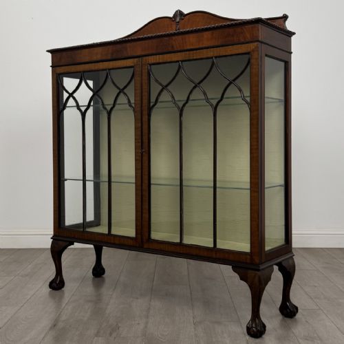 fig 1. A dark mahogany glazed display cabinet featuring gothic astragal door bars, a carved pediment top, and cabriole legs with ball and claw feet.