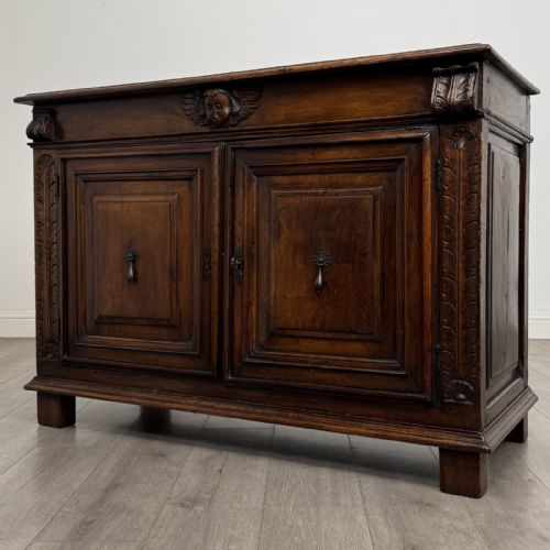 fig 1. A 19th-century French dark walnut sideboard featuring twin panelled doors with drop handles, flanked by fluted pilasters, with a carved winged cherub head centred on the frieze.