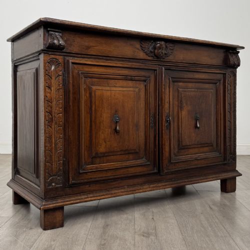 fig 7. A 19th-century French dark walnut sideboard featuring twin panelled doors with drop handles, flanked by fluted pilasters, with a carved winged cherub head centred on the frieze.