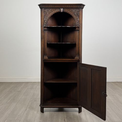 fig 2. A tall dark oak Jacobean style corner cabinet featuring an upper open section with an arched alcove and two shelves above a single panelled cupboard door.