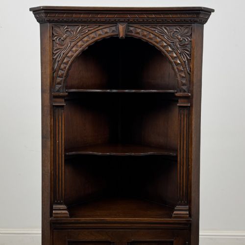 fig 3. A tall dark oak Jacobean style corner cabinet featuring an upper open section with an arched alcove and two shelves above a single panelled cupboard door.